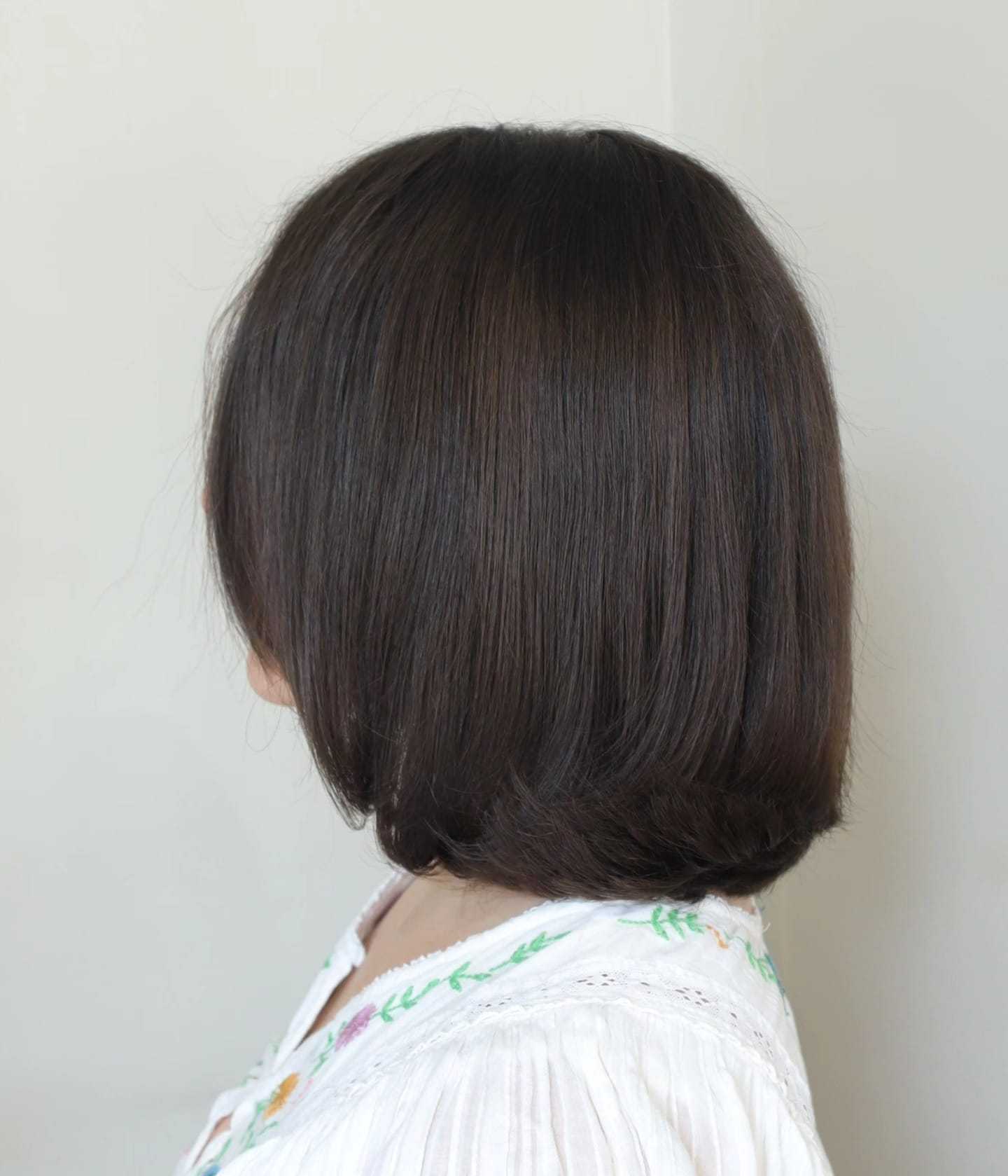 Short brown bob hairstyle with a white embroidered blouse, facing sideways.