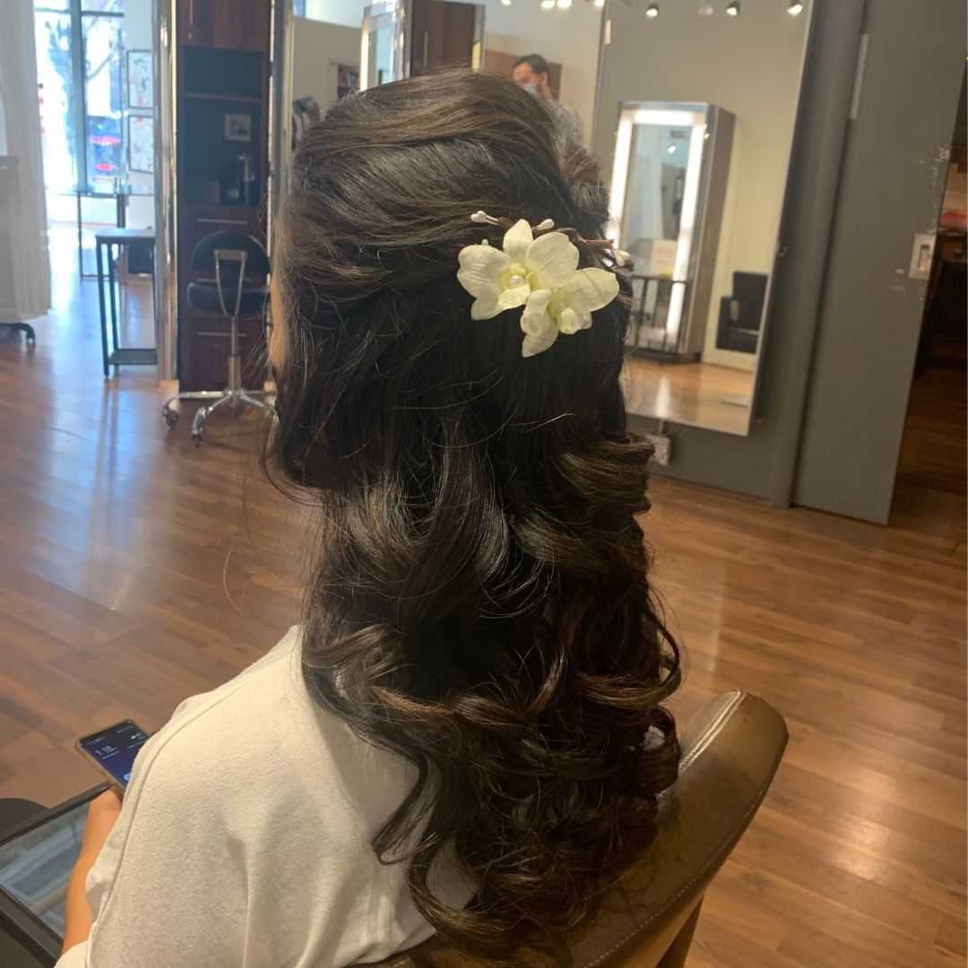 Woman with curled hair and floral accessory seated in a salon.