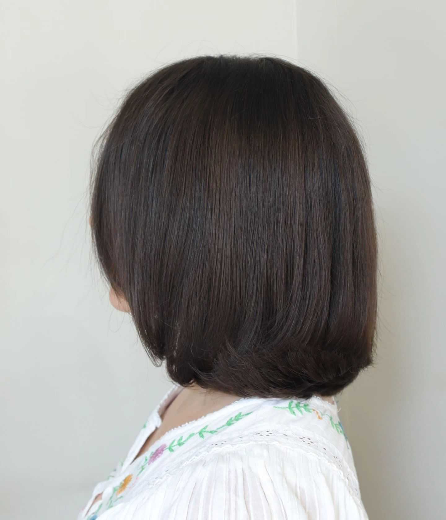 Short brown bob hairstyle with a white embroidered blouse, facing sideways.