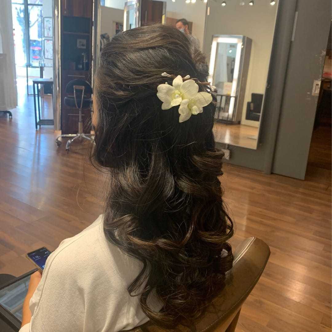 Woman with curled hair and floral accessory seated in a salon.