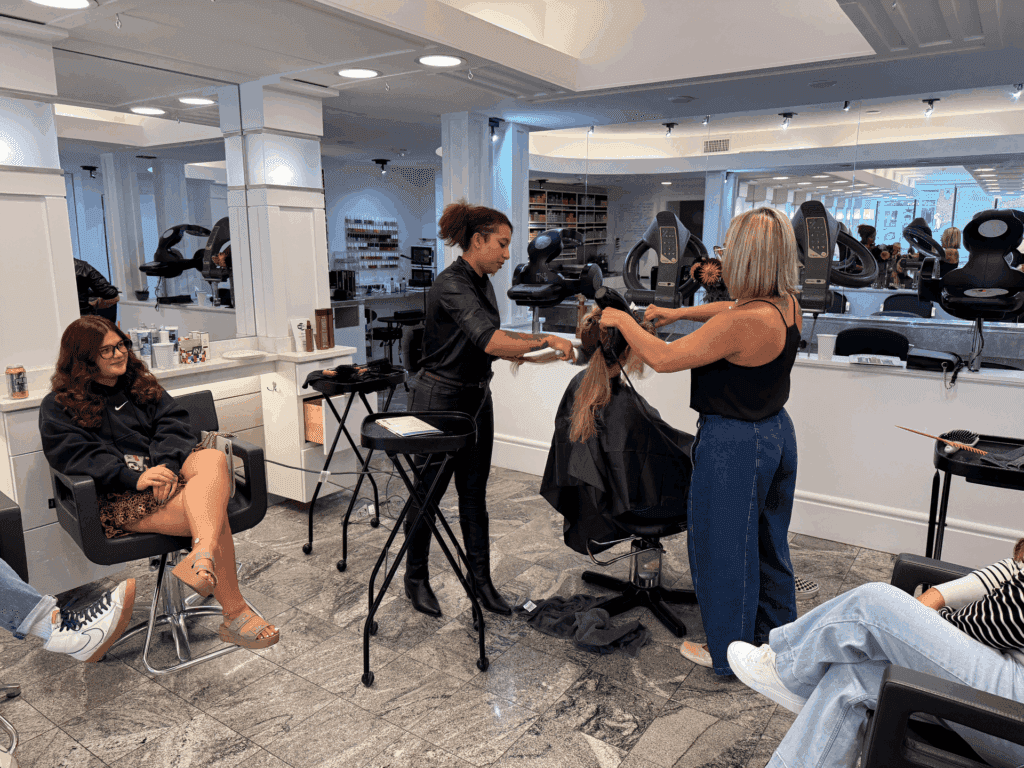 Hair salon with stylists working on a client's hair, and people waiting nearby.